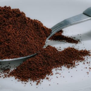 Closeup of aromatic fresh ground coffee powder heaped in silver teaspoon placed on white surface